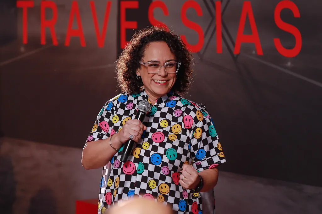 Maryana com Y no palco, em frente a um painel com a palavra Travessias